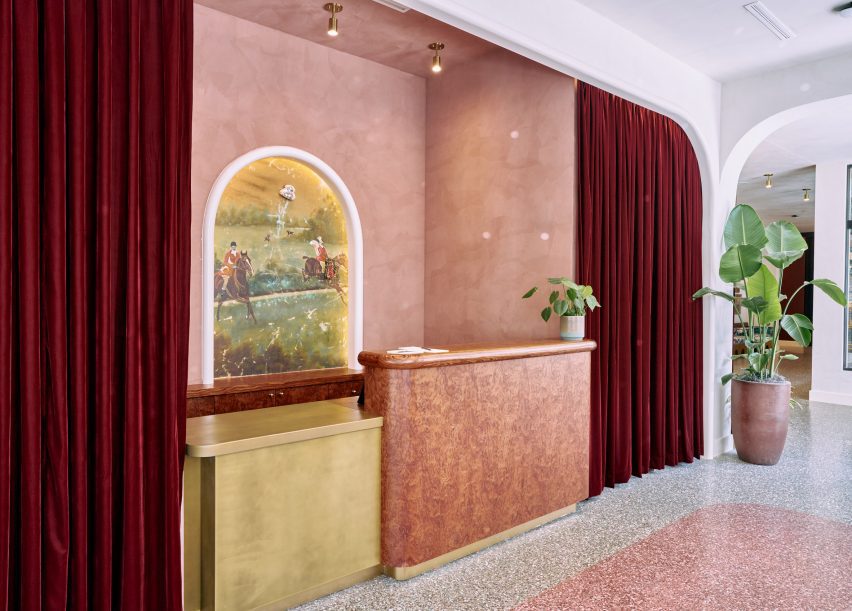 Lobby with pink terrazzo flooring matches the plasterwork behind the reception desk.