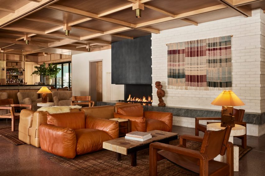 The lobby lounge featuring earth-toned furniture, a gridded wood ceiling, and an open fireplace.