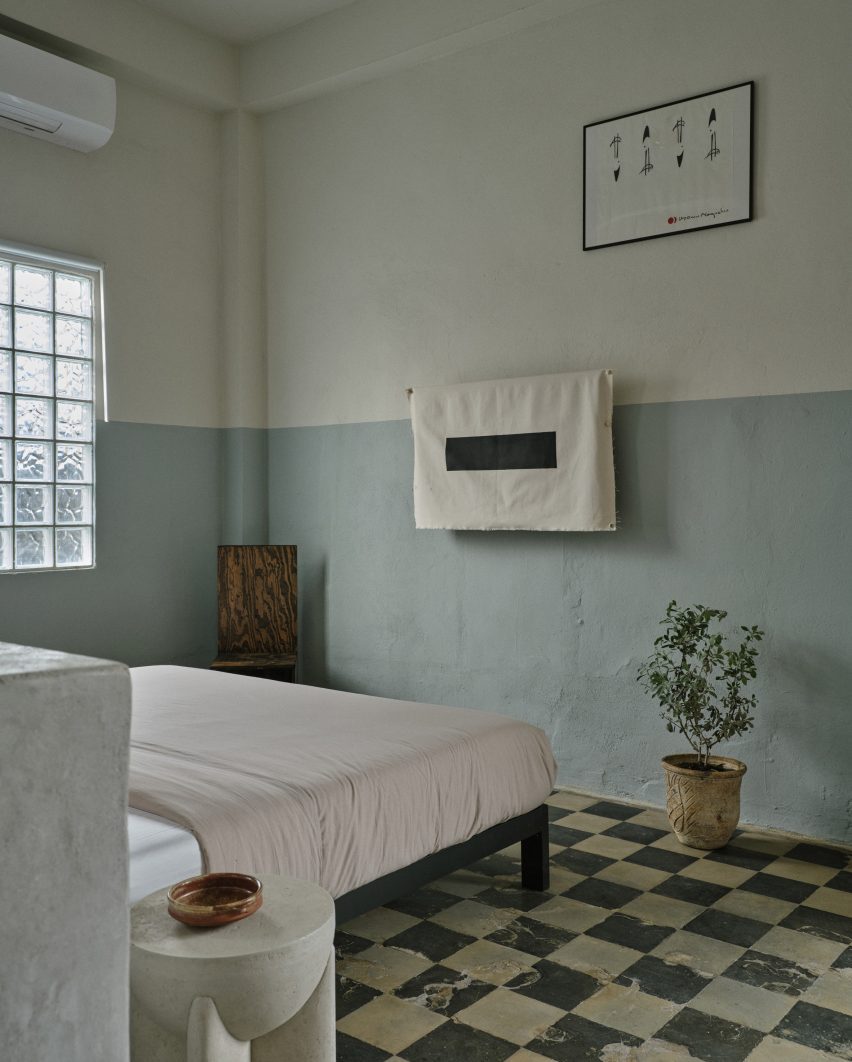 The studio apartment has vintage floor tiles, a central bed, and blue-beige walls.