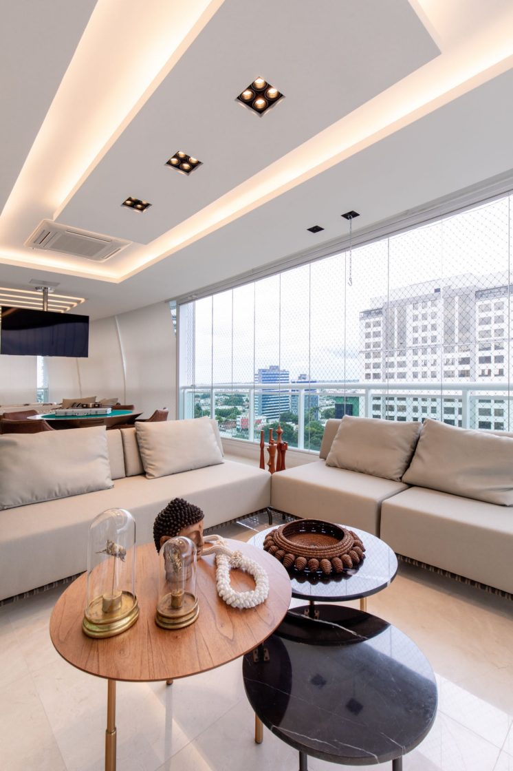 Sala com sofá acinzentado e mesas de centro com objetos decorativos.