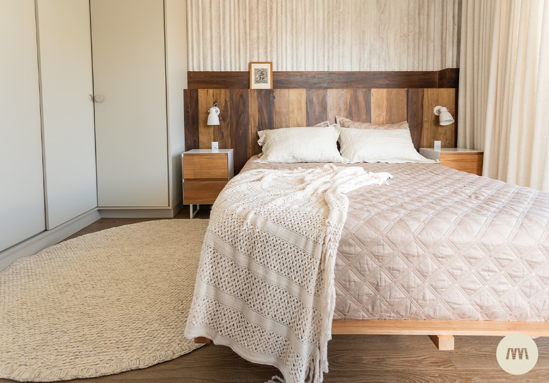 Quarto em tons madeira, bege e offwhite, cortinas fluidas e mesas de cabeceira em madeira, pendentes metálicos sobre cabeceira em madeira.