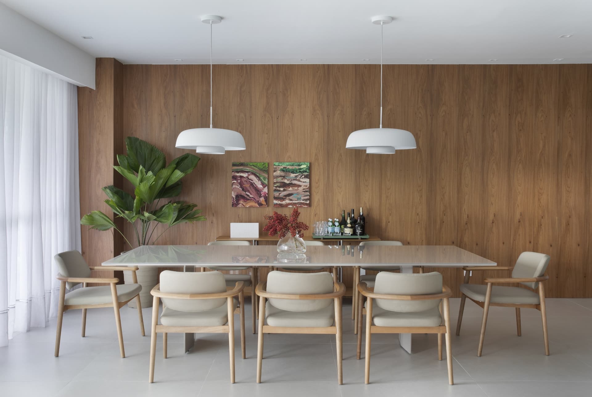 Sala de jantar com mesa em porcelanato, paredes com porcelanato com textura de madeira, dois pendentes, cortinas claras e vaso com planta próximo da parede.