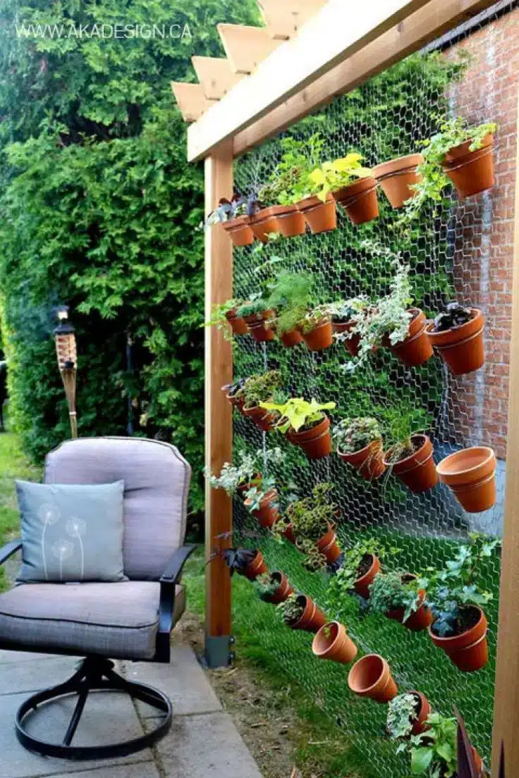 Parede verde feita com tela de aço, servindo como suporte para vasos de plantas.