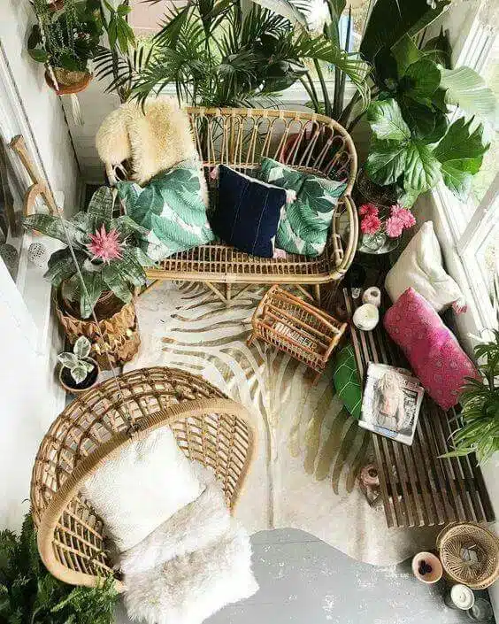 Varanda decorada com cadeira de balanço, palmeiras e almofadas coloridas, criando um ambiente aconchegante.