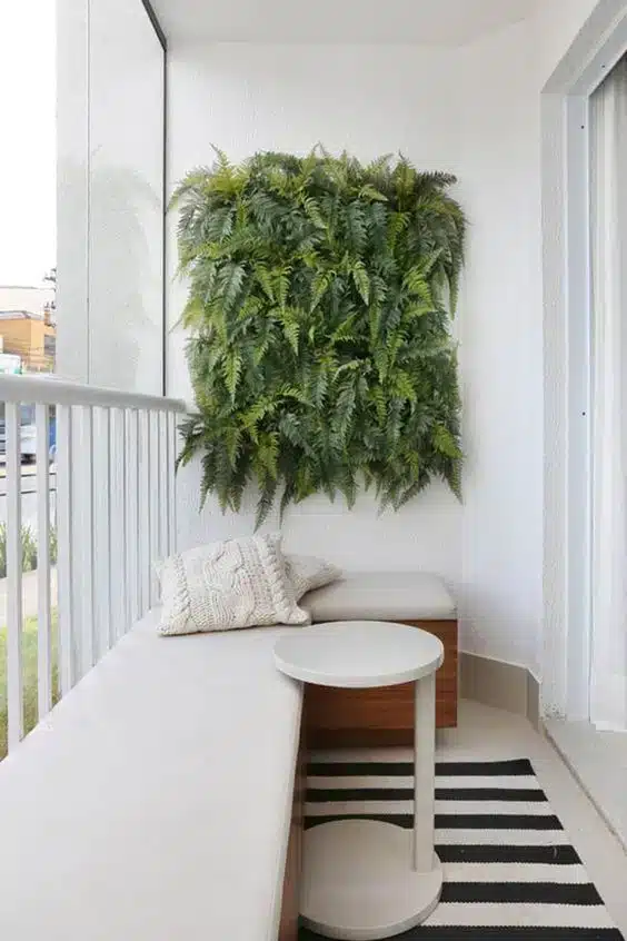 Varanda com tapete listrado, sofás de canto e mesinha de apoio, decorada com flores e samambaias.