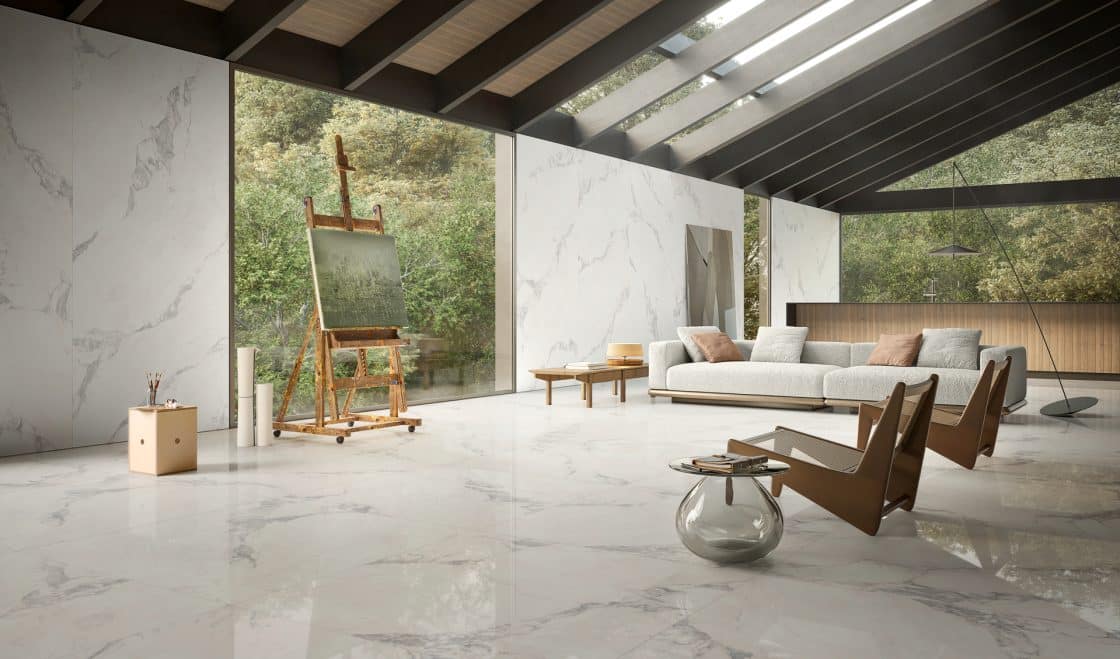 Ambiente de estar com revestimento que reproduz mármore, um cavalete de pintura, cadeiras, mesas e sofá.
