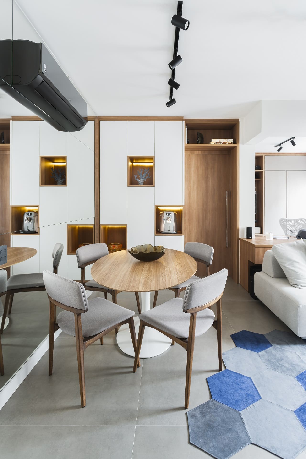 Sala de jantar pequena em tons de branco, cinza e madeira, com tapete com hexágonos azuis (Projeto: Rico Mendonça)