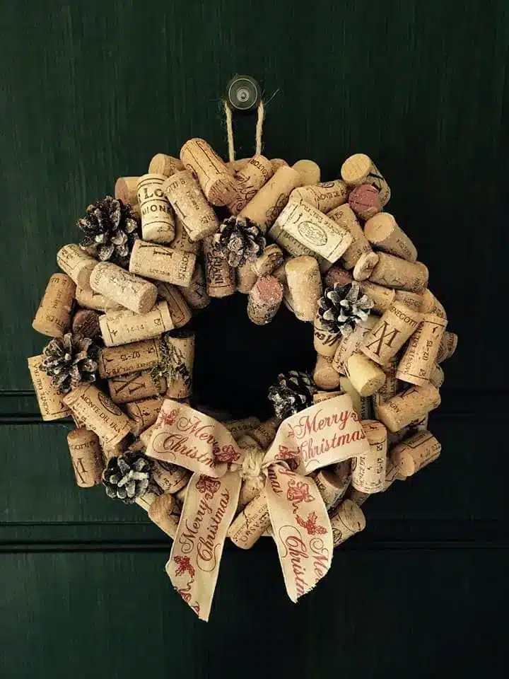 Guirlanda feita com rolhas de vinho, decorada com fitas e um sino dourado.