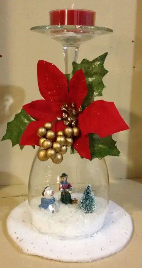 Taça de vinho decorativa, contendo pedrinhas brancas e uma mini árvore de Natal.