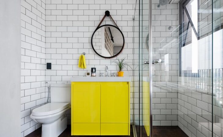 No banheiro o espelho é fundamental para a composição. O formato redondo compõe o visual moderno e urbano com os azulejos de metrô e o amarelo em destaque.