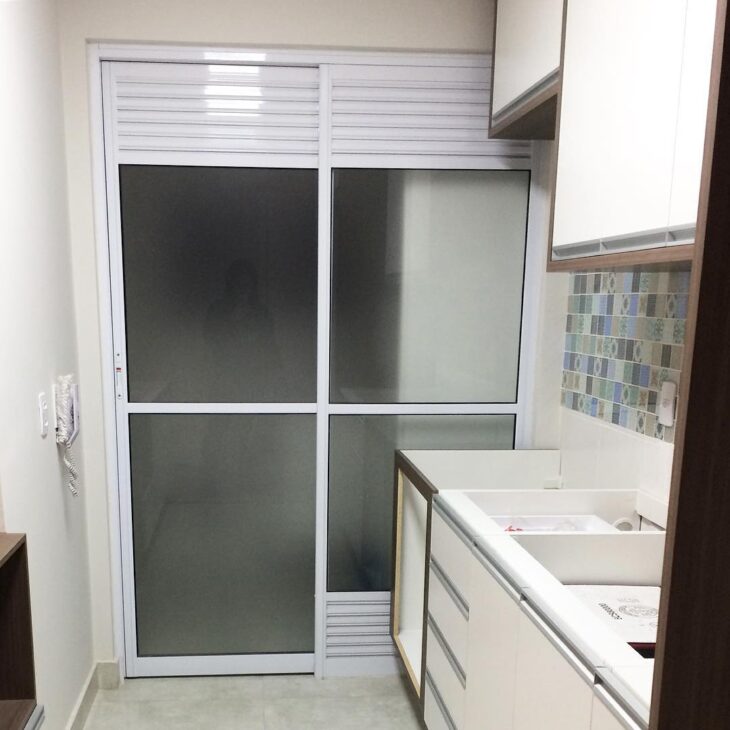 Porta de vidro com adesivo jateado para disfarçar itens de limpeza na lavanderia.